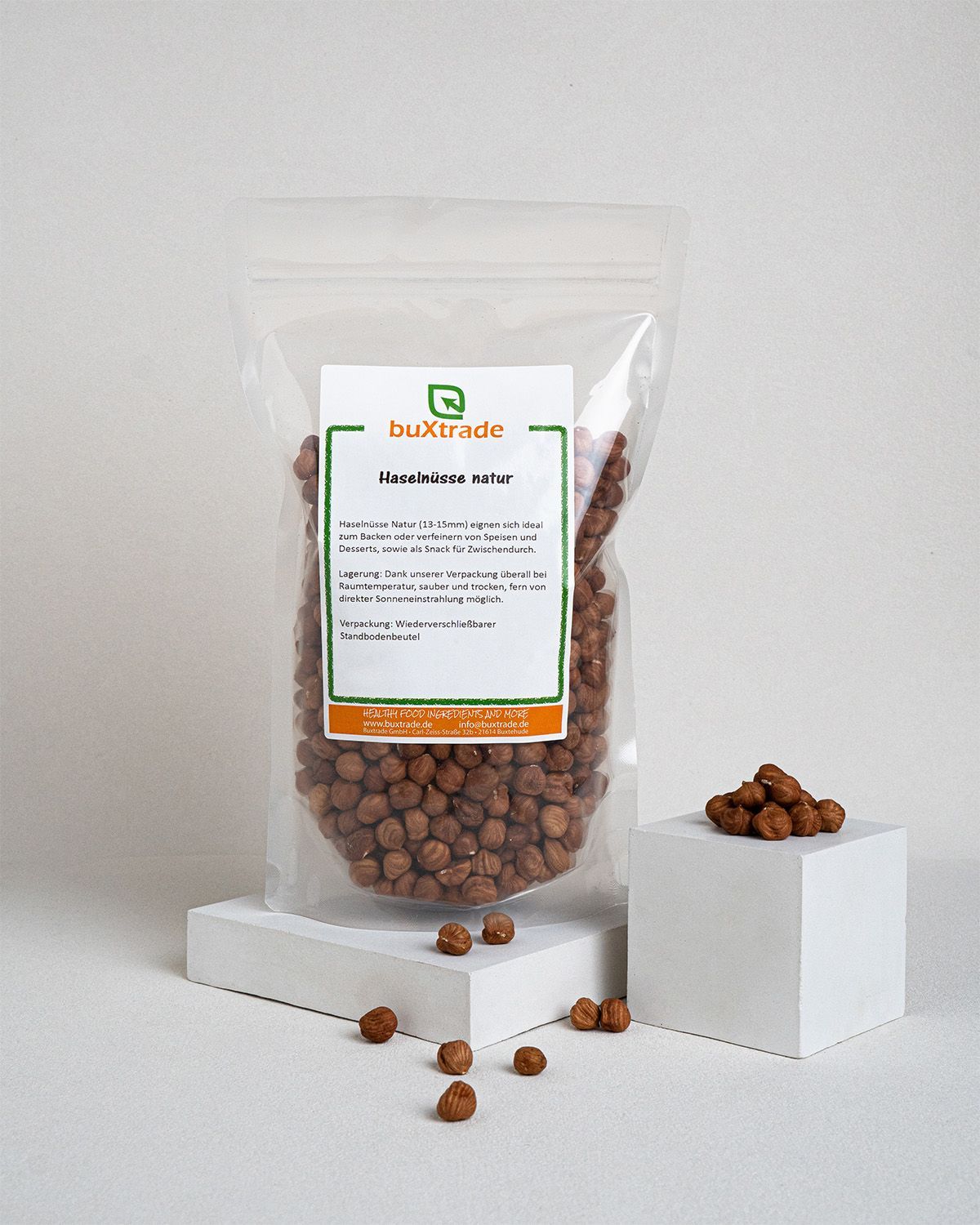Transparente Verpackung mit Haselnüssen. Aufkleber mit Produktinformationen: buXtrade Haselnüsse natur. Einzelne Nüsse daneben.