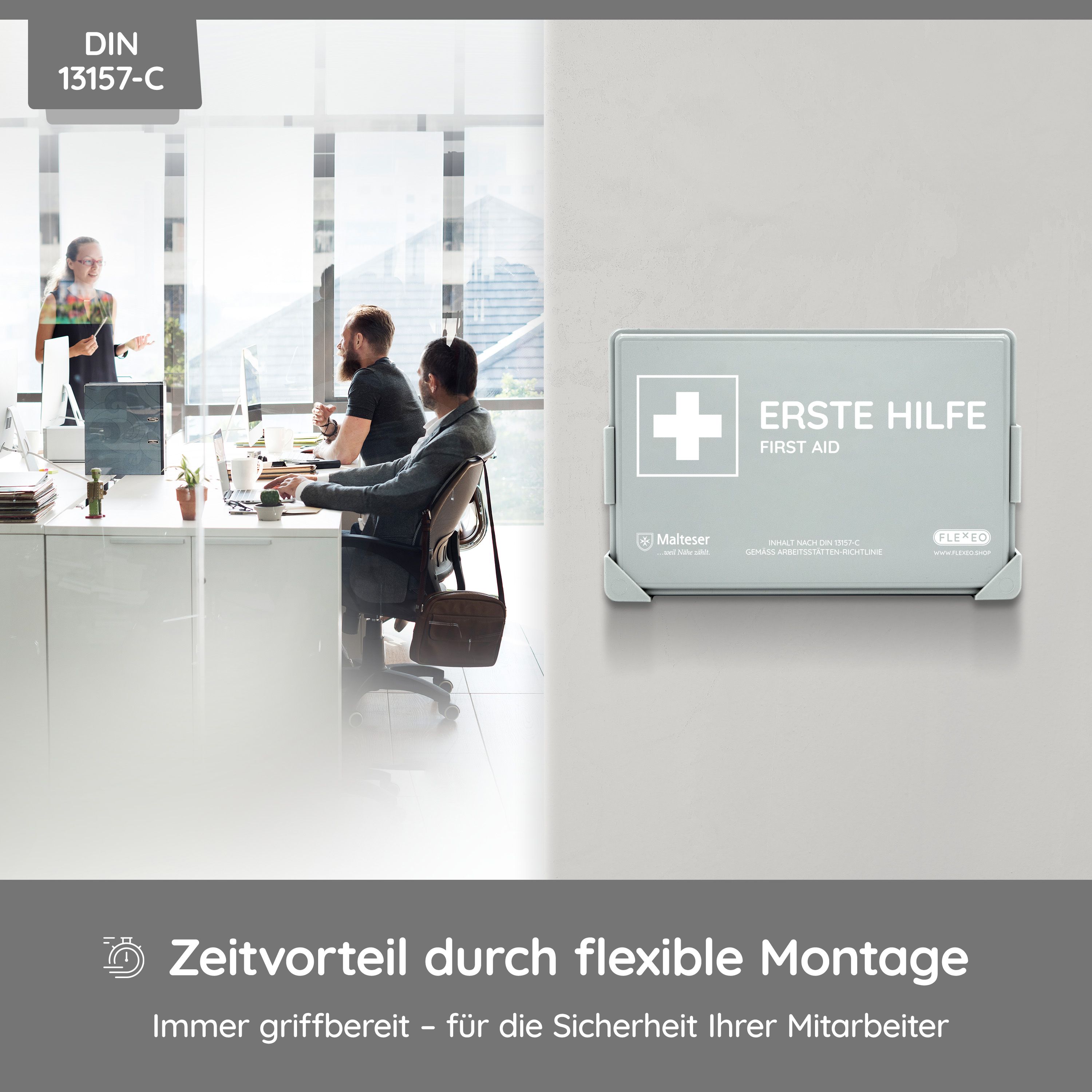 Grauer Verbandkasten mit weißem Kreuz und Aufschrift "ERSTE HILFE". DIN 13157-C. Im Hintergrund Büroumgebung.