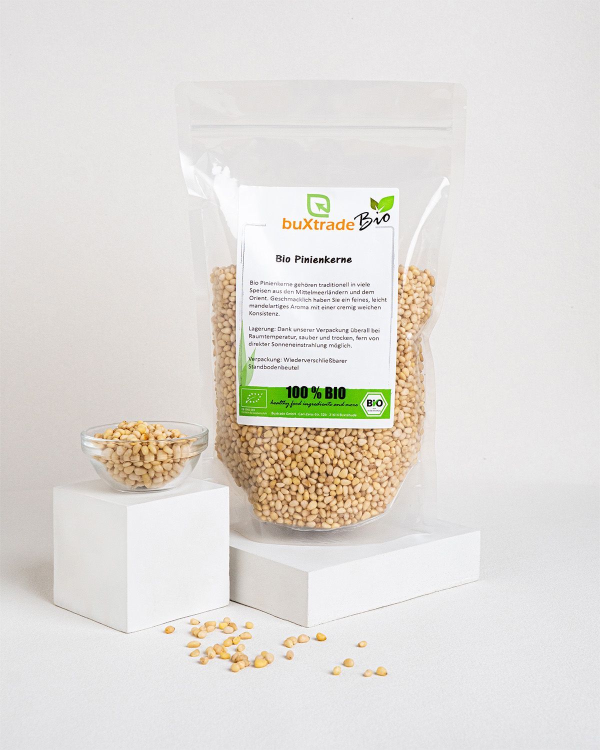 Transparente Verpackung mit Pinienkernen, daneben eine Schale mit Pinienkernen. Aufdruck: buXtrade Bio, Bio Pinienkerne, 100% BIO-Siegel.