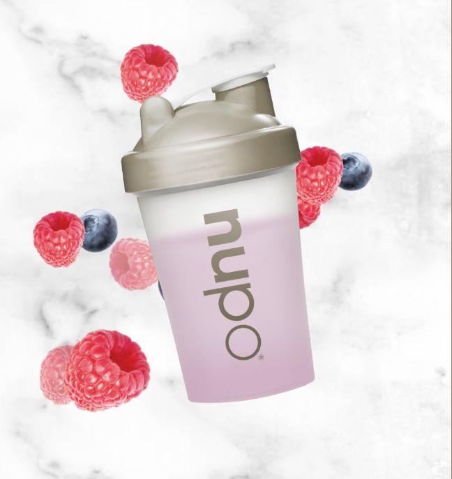 Shaker mit Flüssigkeit und Früchten. Himbeeren und Blaubeeren umgeben den Shaker.