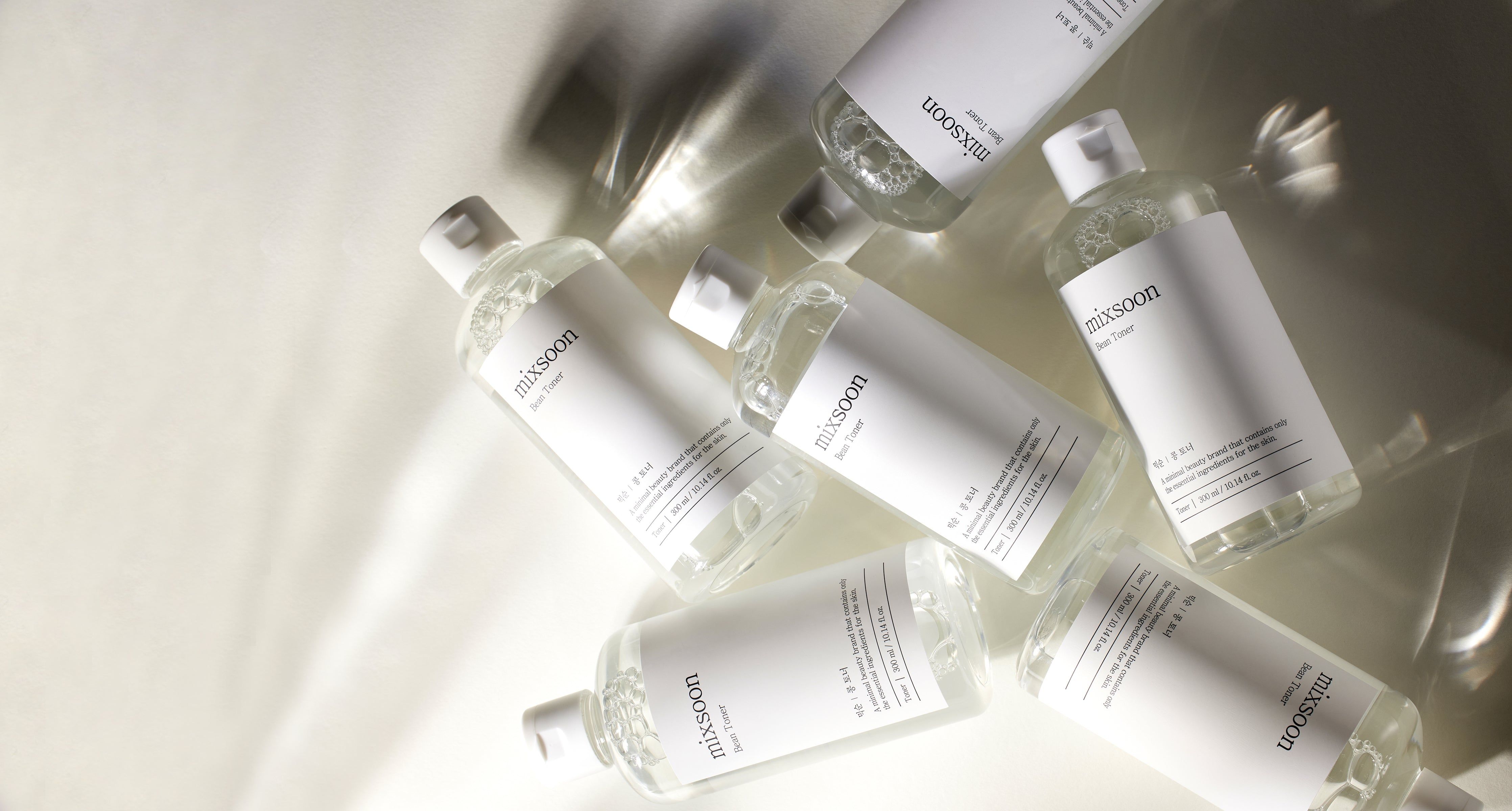 Mehrere Flaschen mixsoon Bean Toner liegen auf einer glänzenden Oberfläche. Weiße Etiketten.