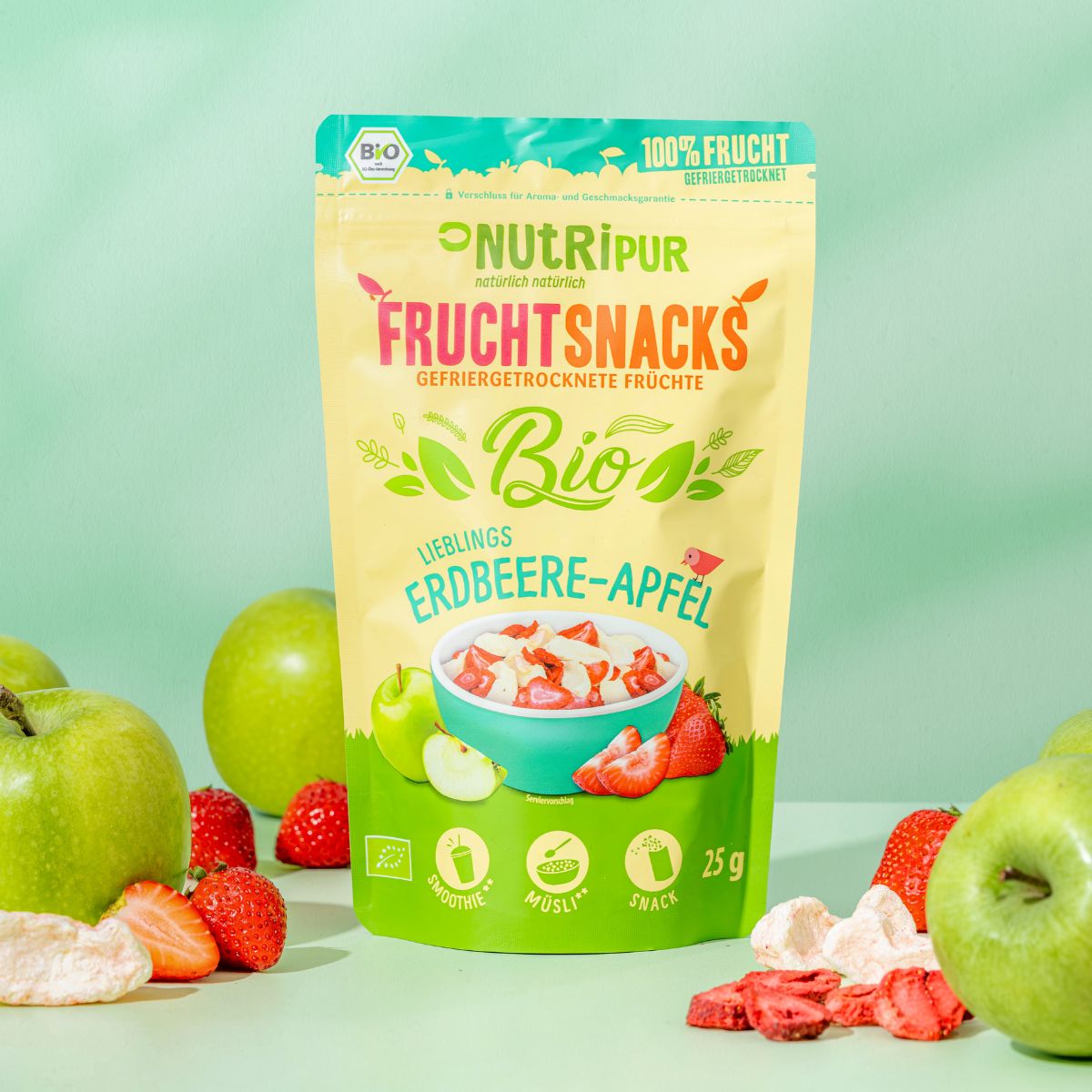 Beutel mit gefriergetrockneten Erdbeere-Apfel-Früchten, umgeben von Äpfeln und Erdbeeren. Bio-Siegel und 100% Frucht-Logo.