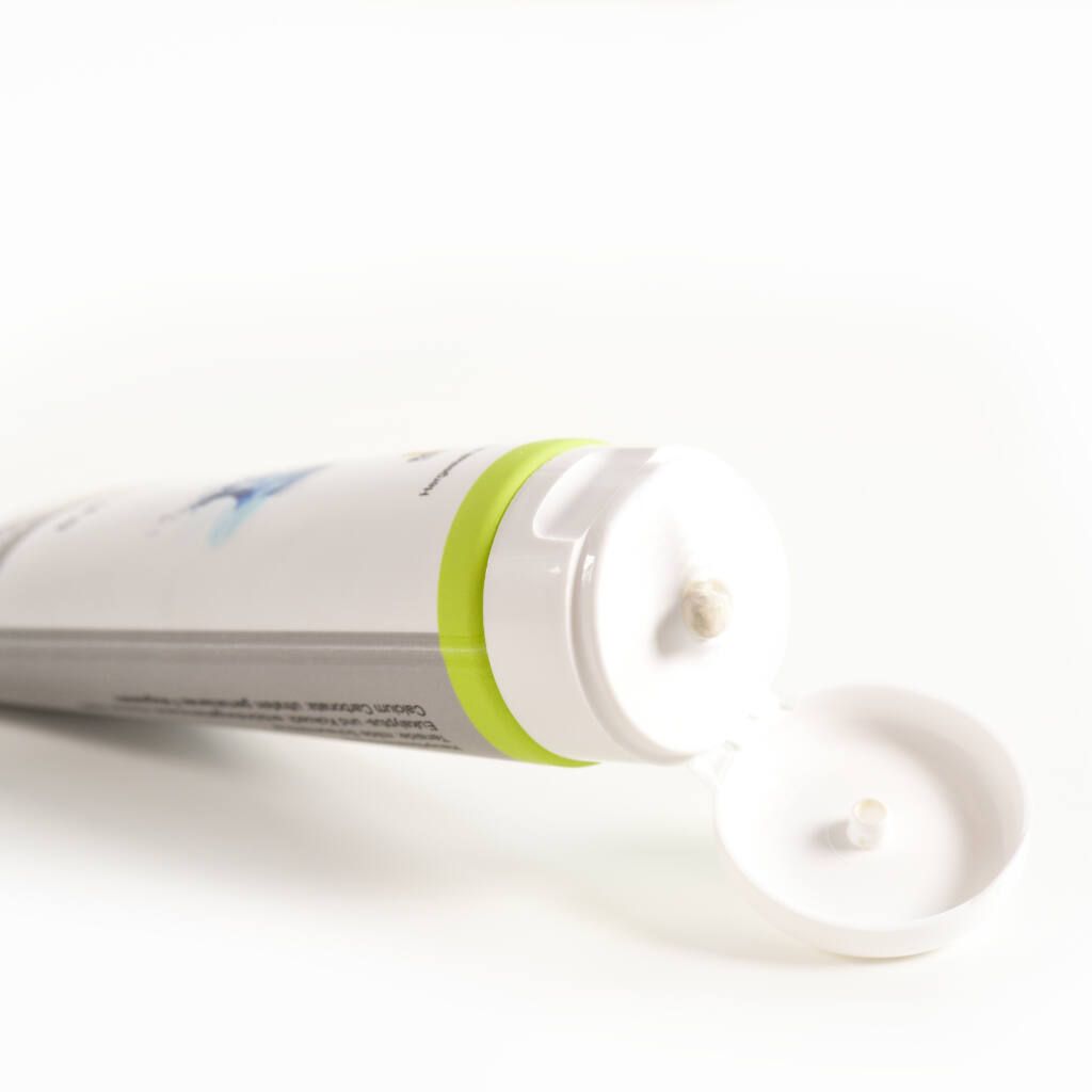Geöffnete Tube Zahnprothesenpaste. Weiße Tube mit grünem Ring. Paste tritt aus der Öffnung aus.