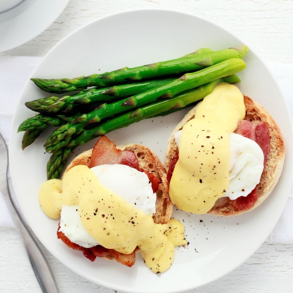 Teller mit Eggs Benedict und Spargel. Zwei Eier Benedict mit Sauce Hollandaise. Grüner Spargel.