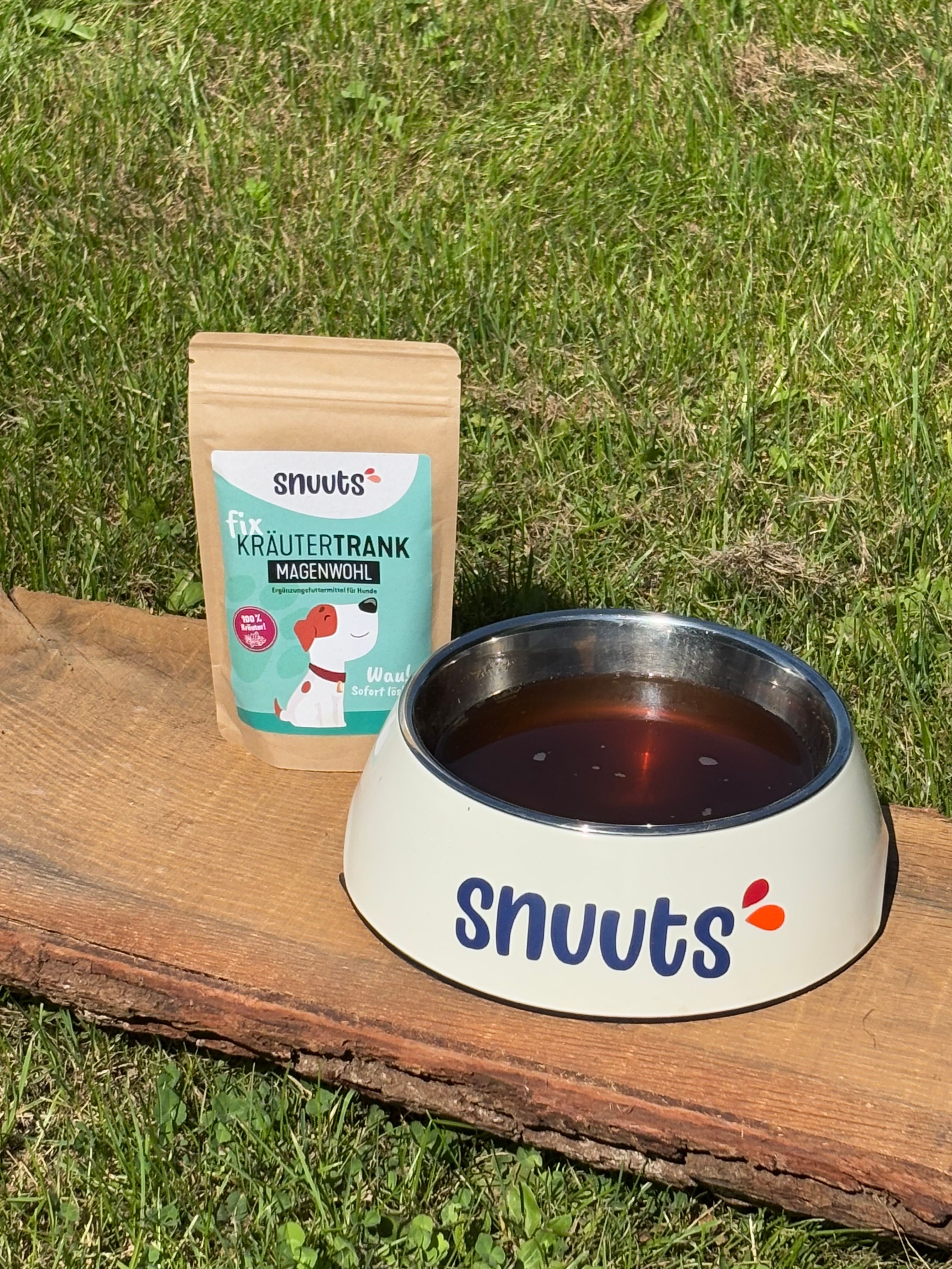 Beutel und Napf mit Flüssigkeit. Aufschrift: snuuts. Napf mit Flüssigkeit. Aufschrift: snuuts. Auf Holzbrett vor Gras.