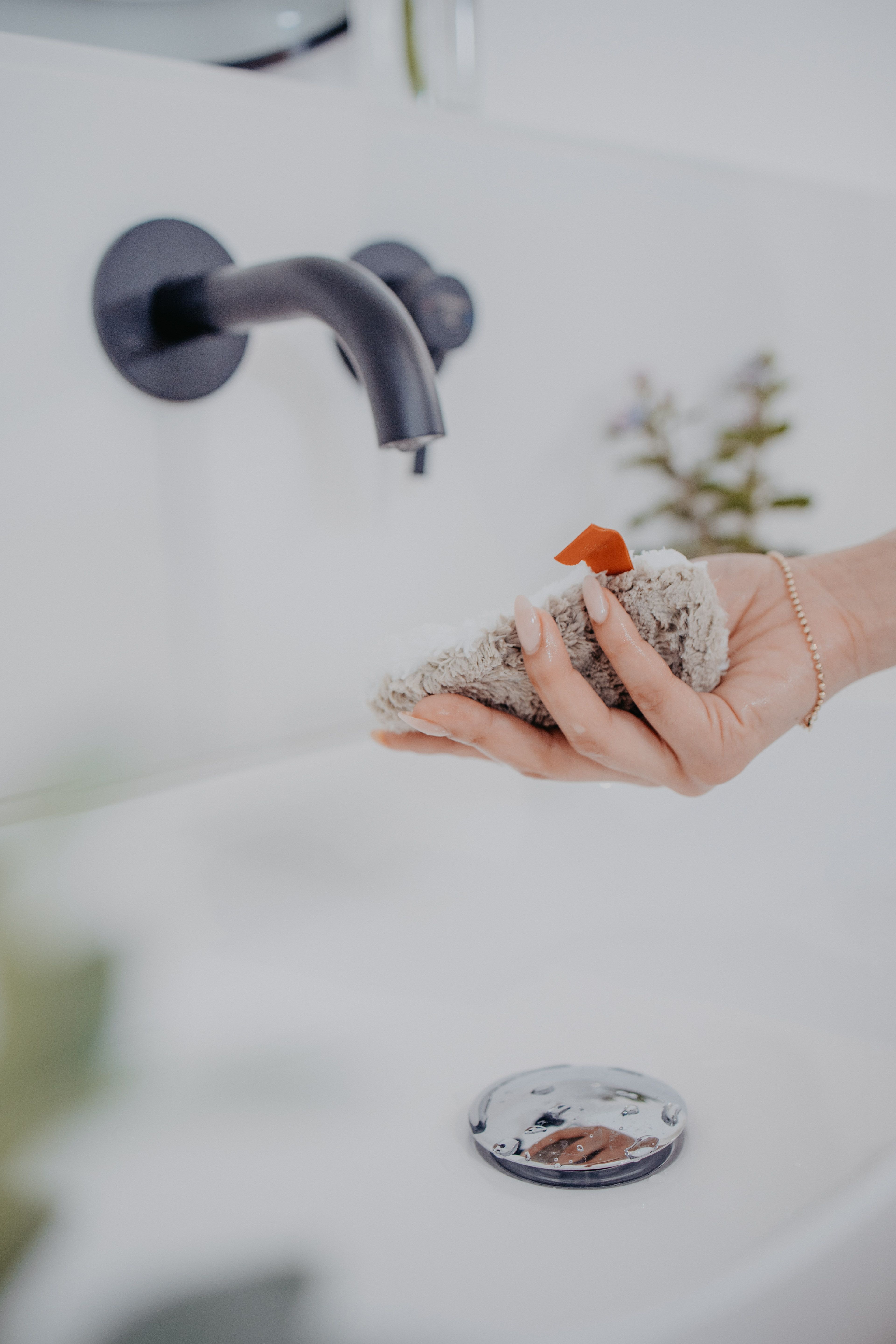 Hand hält beiges Abschminkpad über Waschbecken. Wasserhahn im Hintergrund.