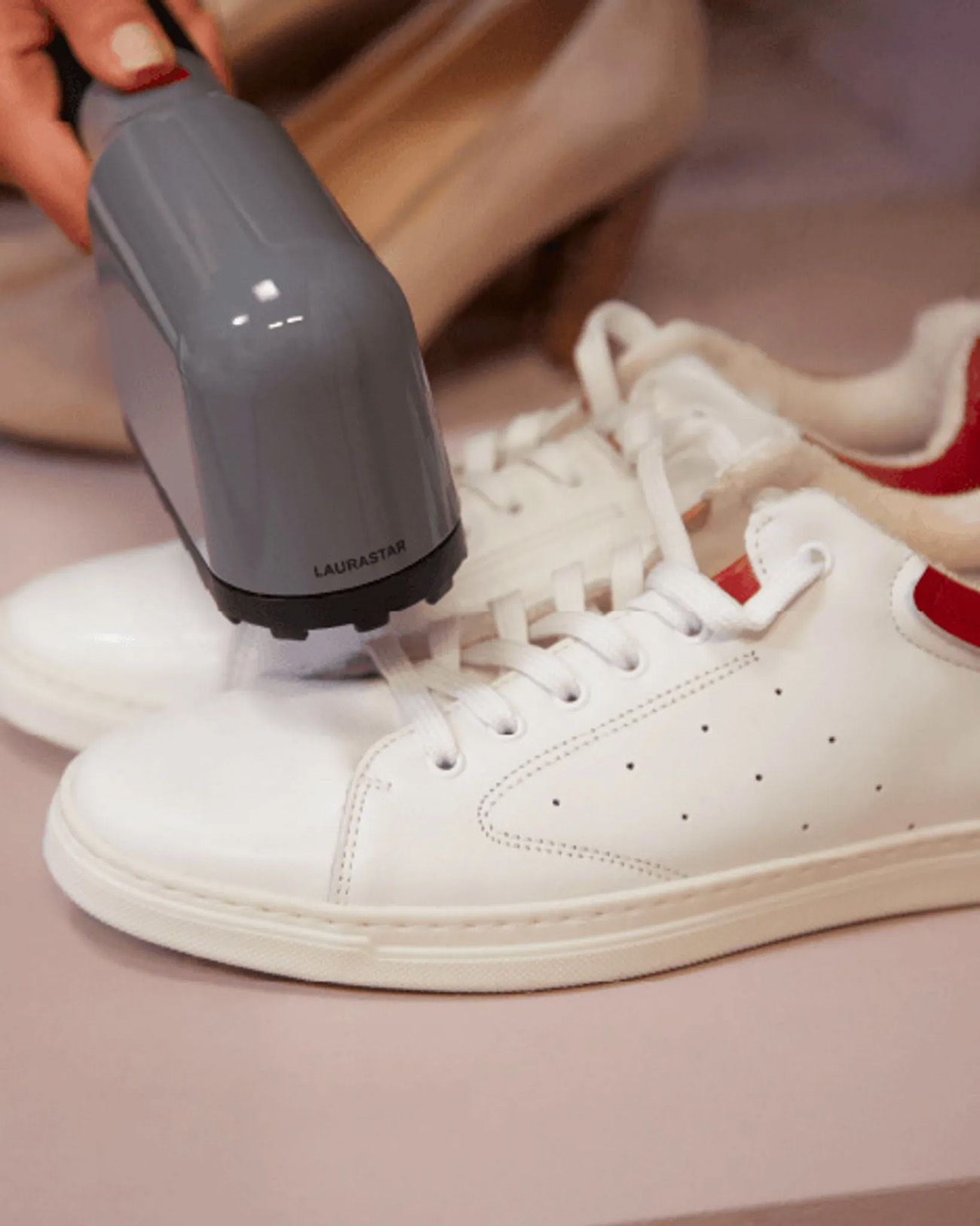 Grauer Dampfreiniger auf weißen Schuhen. Schwarzer Griff. Dampf tritt aus. Hand hält das Gerät. LAURASTAR.