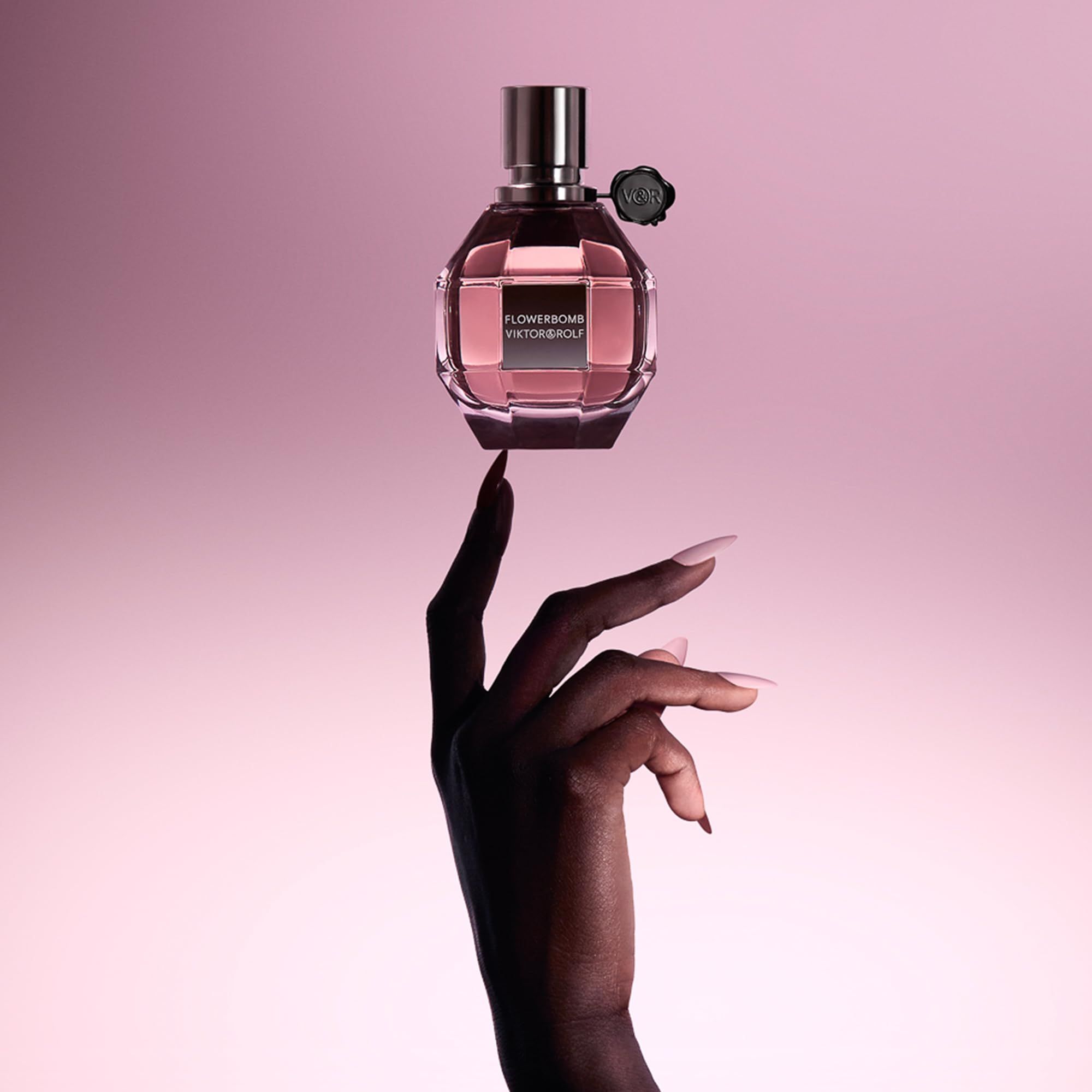 Rosa Flakon auf einer Hand. Roségoldfarbener Verschluss. Schwarzer Verschluss mit Logo. Aufschrift: FLOWERBOMB VIKTOR & ROLF.