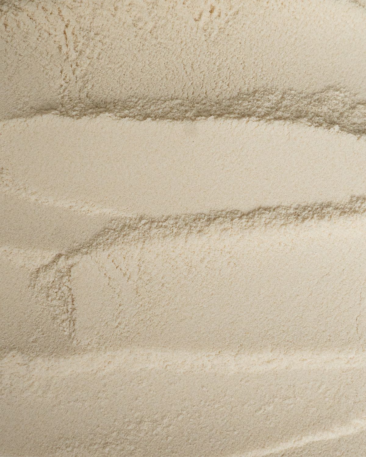 Nahaufnahme von feinem, hellem Xanthan Gum Pulver mit wellenförmigen Texturen.