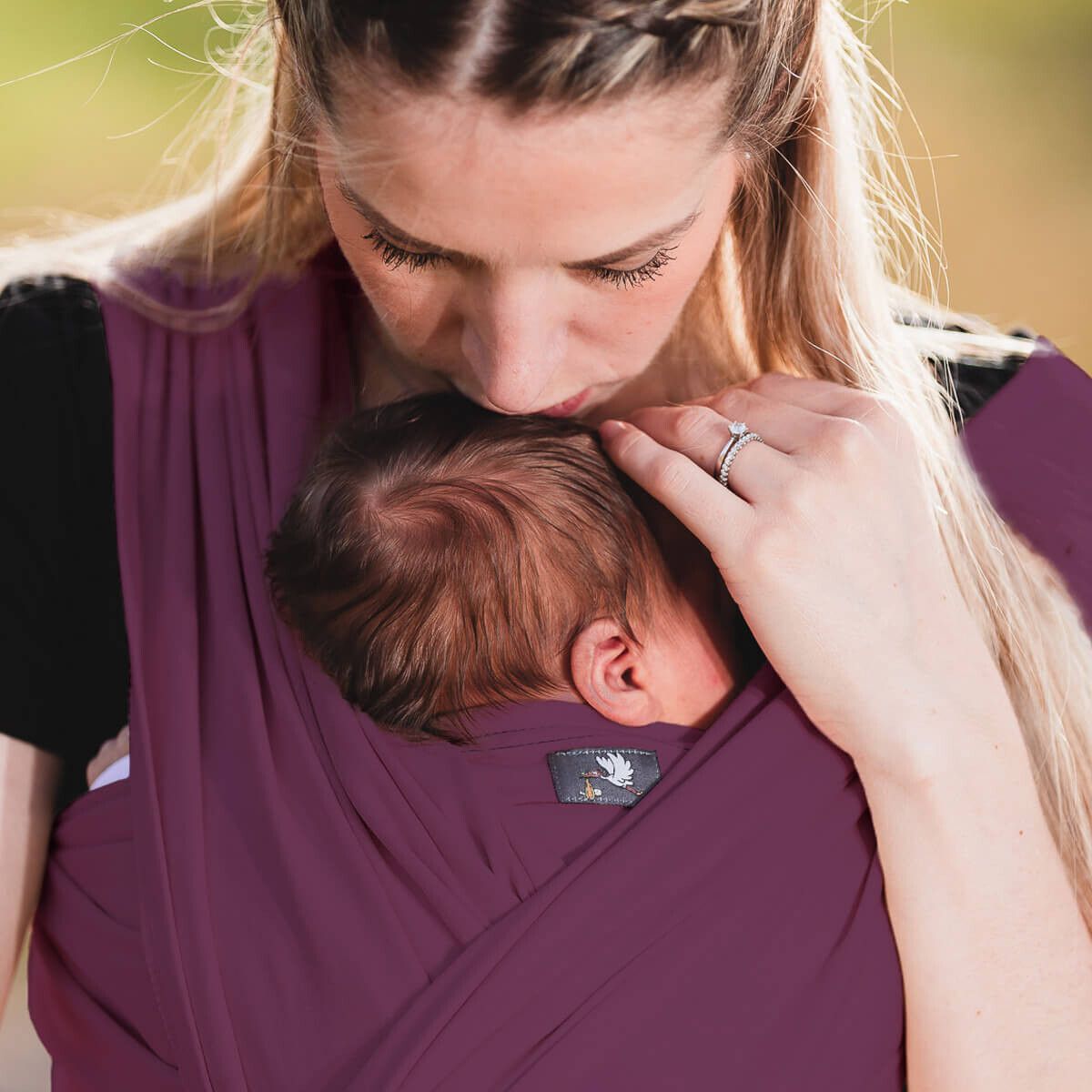 Frau mit Baby in auberginefarbenem Tragetuch. Baby im Tuch. Logo-Etikett. HOPPEDIZ.