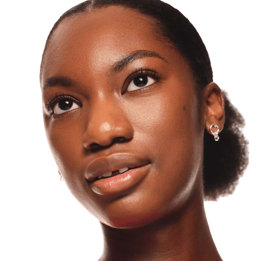 Porträt einer Frau mit dunkler Haut. Sie hat dunkle Augenbrauen und trägt Ohrringe.