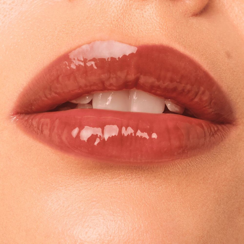 Nahaufnahme von Lippen mit glänzendem Lipgloss. Die Lippen sind in einem bräunlichen Farbton gehalten. Zähne sind sichtbar.