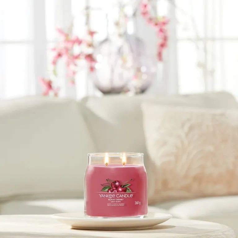 Rote Duftkerze auf Teller. Kirsch-Etikett, zwei Dochte. Auf Tisch vor Sofa. Yankee Candle Black Cherry.