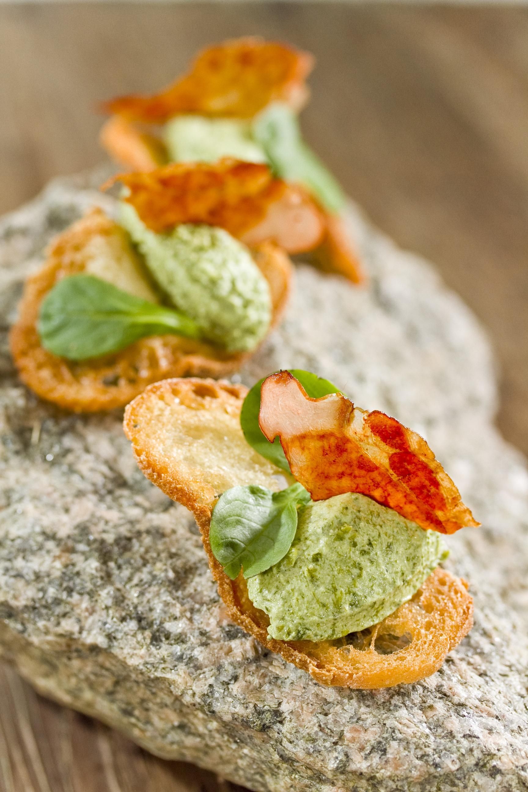 Tapas auf Stein. Basis aus geröstetem Brot, mit Kräutercreme und Fleisch belegt, mit Basilikum dekoriert.