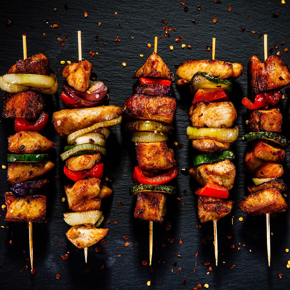 Fünf Spieße mit Fleisch und Gemüse. Fleischstücke, Zwiebeln, Paprika und Zucchini auf Holzspießen. Auf schwarzem Untergrund.