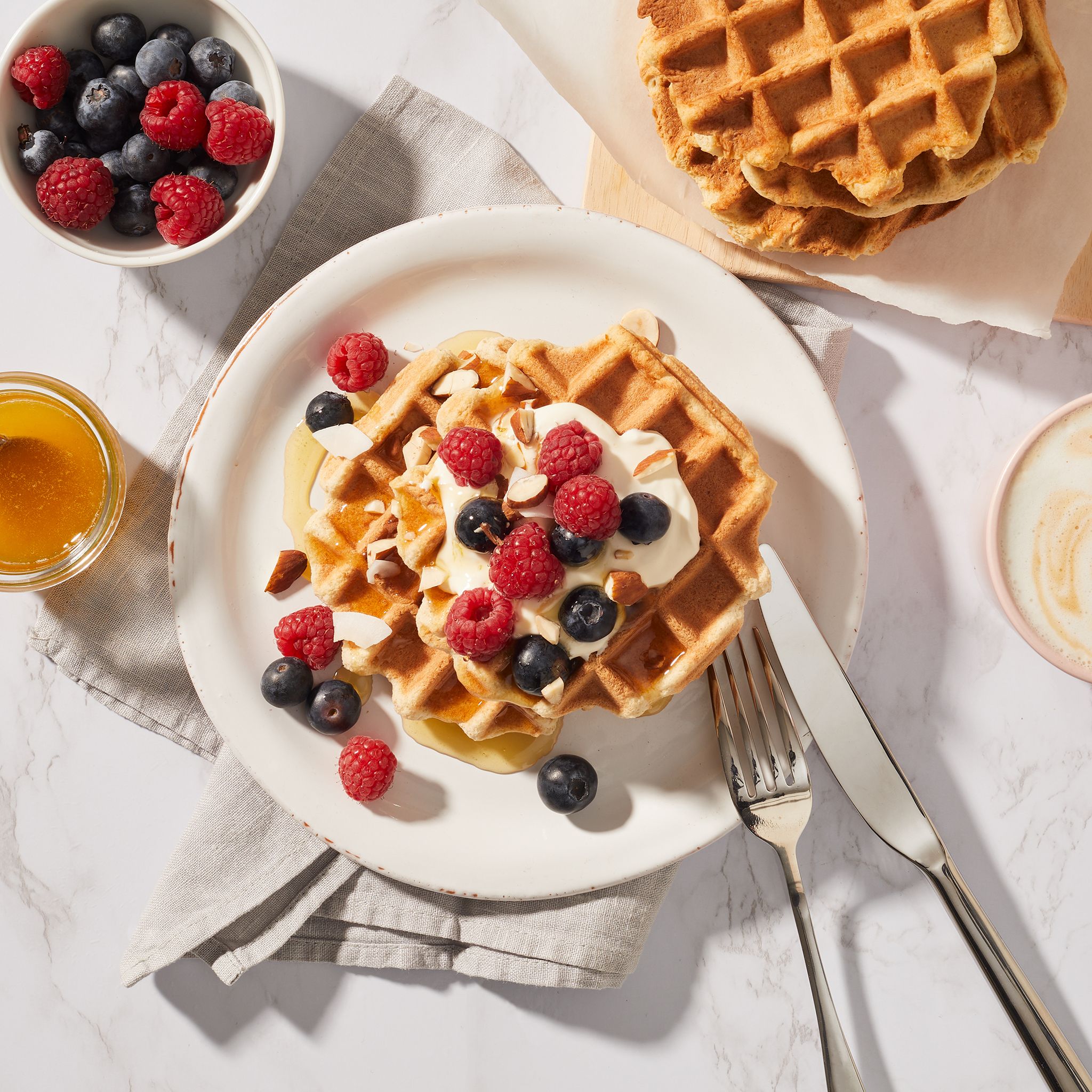 Waffeln auf Teller mit Beeren und Nüssen. Honig und Kaffee daneben. Draufsicht.