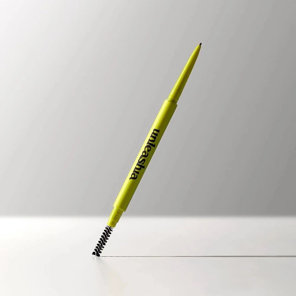 Ein spitzer, gelber Augenbrauenstift mit Bürstenaufsatz. Der Markenname 'unleashia' ist auf dem Stift aufgedruckt.