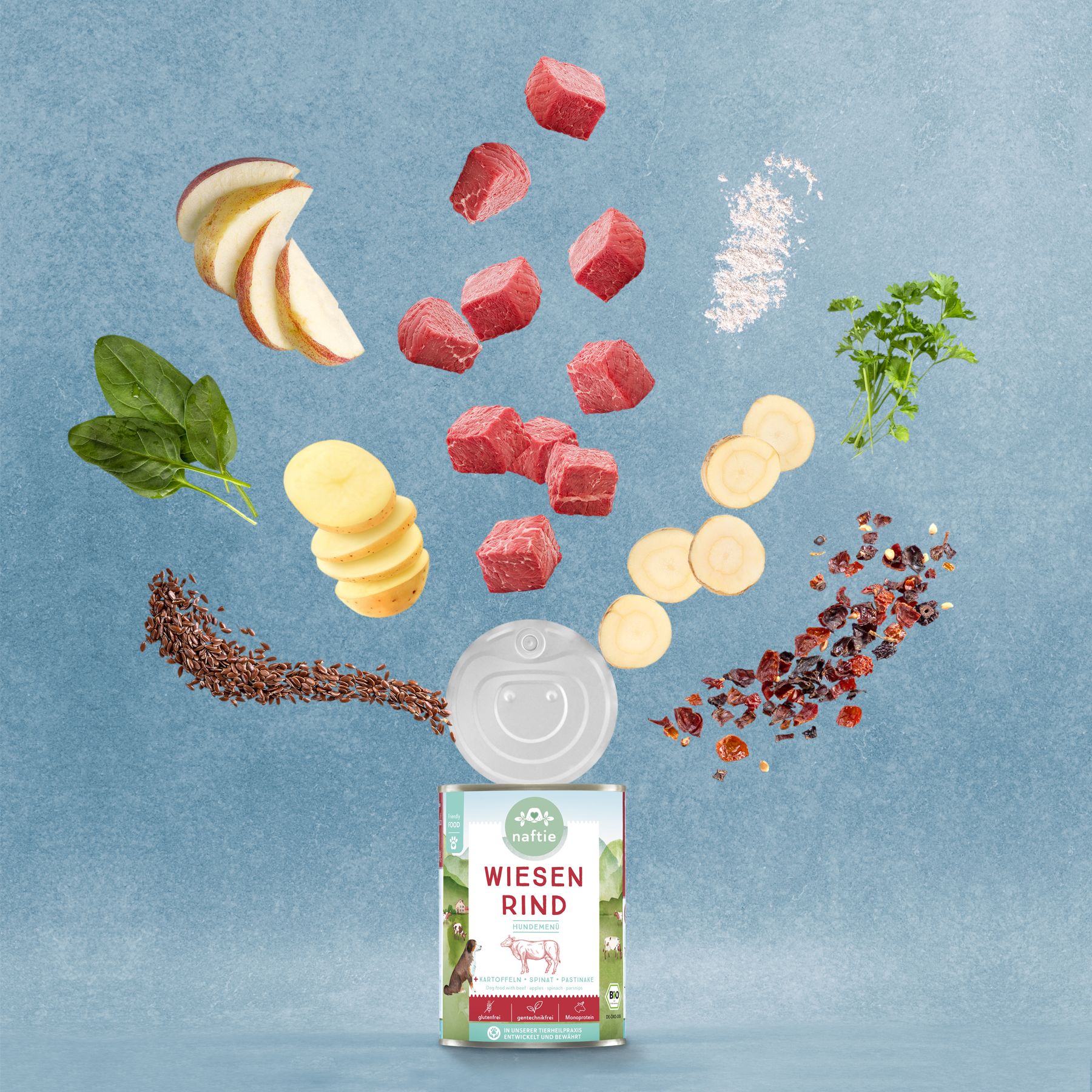Dose naftie Bio Wiesen Rind mit Zutaten: Fleischwürfel, Apfel, Spinat, Kartoffeln, Petersilie, Leinsamen, Pastinake, Hagebutten. Blauer Hintergrund.