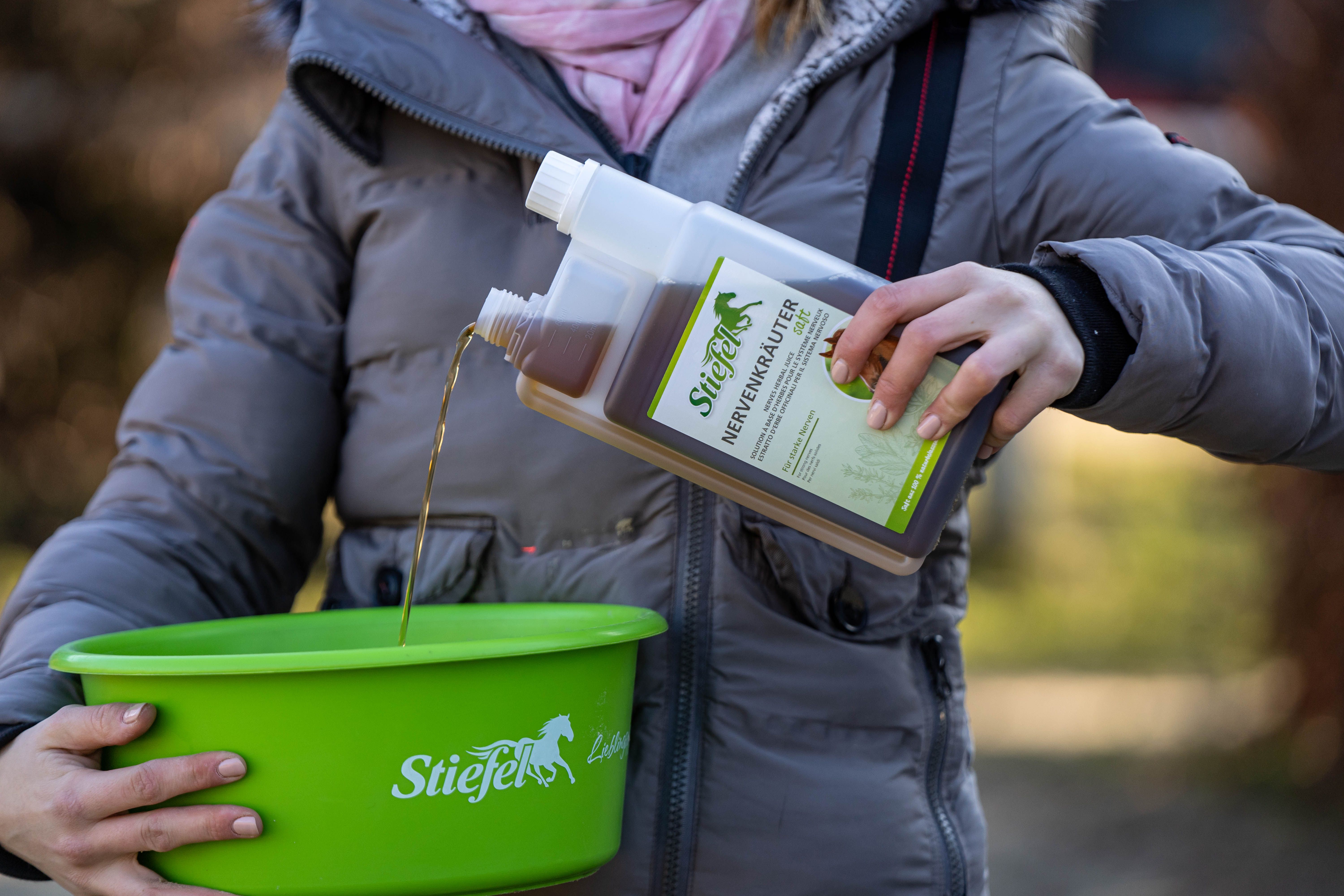 Person gießt Stiefel Nervenkräutersaft aus einer Flasche in eine grüne Schüssel. Auf der Schüssel steht Stiefel.