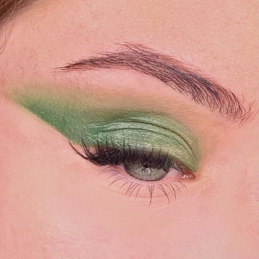 Grüner Lidschatten auf einem Auge. Augenlid und Lidfalte betont. Wimpern und Augenbraue sichtbar.