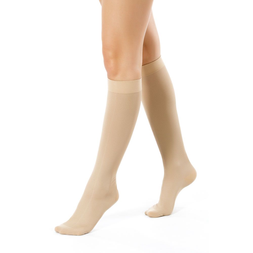 Beige Kompressionsstrümpfe, knielang, geripptes Design. Auf weißem Hintergrund, von den Knien abwärts gezeigt.