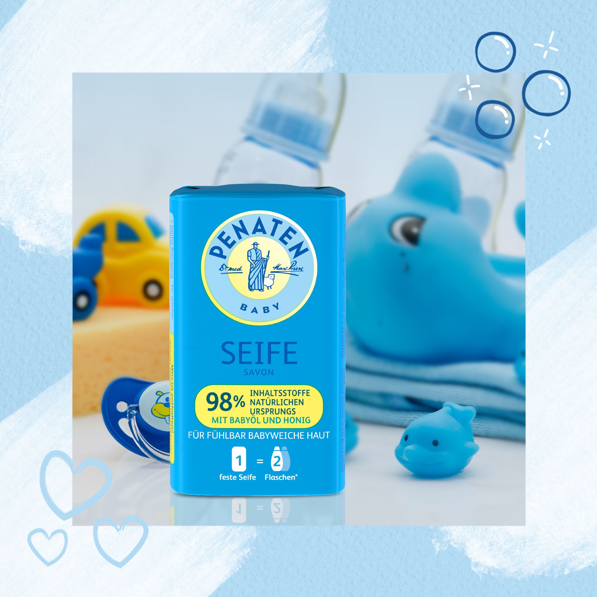 Blaue Seife-Verpackung mit Spielzeug. Aufschrift: Penaten Baby Seife, 98% natürliche Inhaltsstoffe, mit Babyöl und Honig. 1=2 feste Seifen.