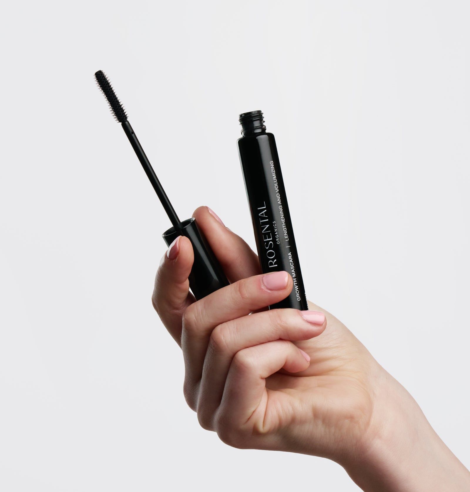 Schwarze Mascara-Tube mit Bürste in einer Hand. Produktname: Rosental Organics Growth Mascara. Weißer Hintergrund.