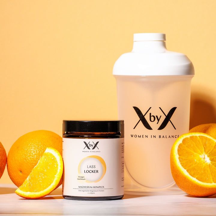 Behälter und Shaker mit Produkt. Orangen und eine halbe Orange liegen daneben. Aufschrift: XbyX WOMEN IN BALANCE.