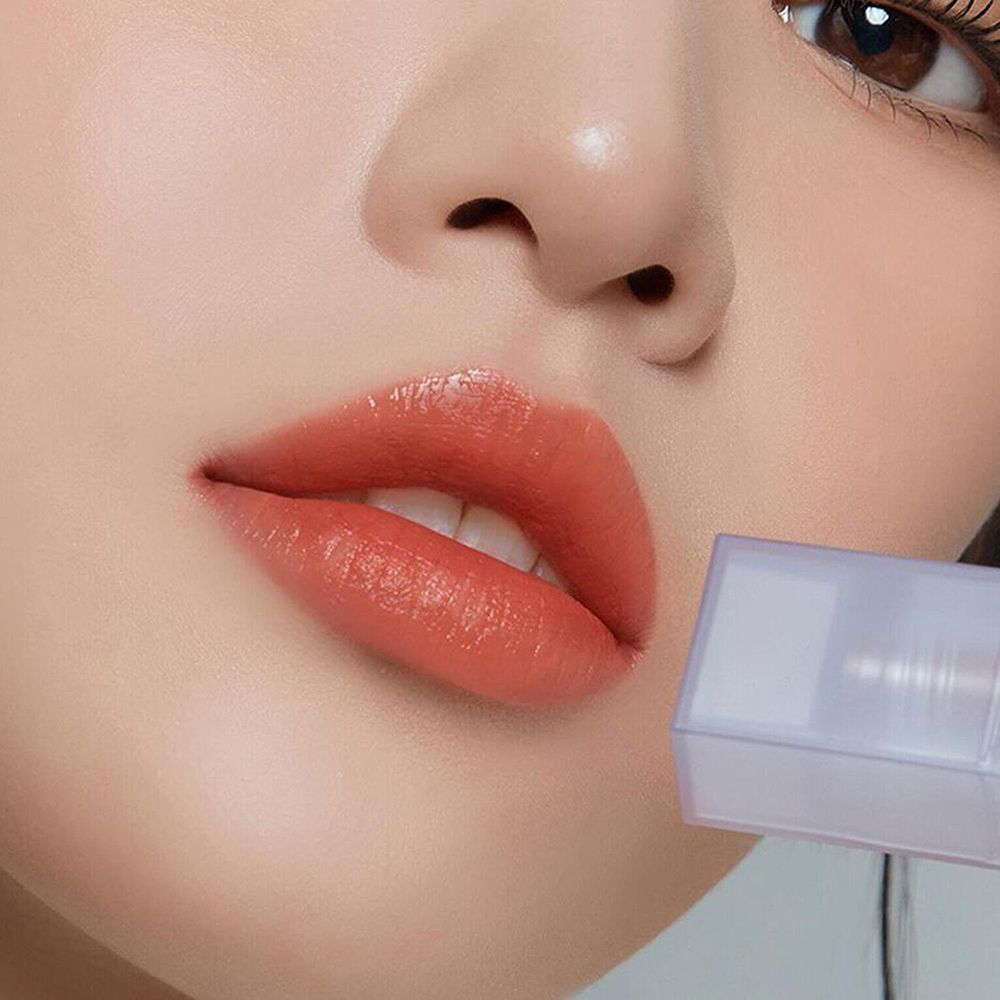 Nahaufnahme von Lippen, die mit Apricot-Nudismus-Lipgloss bedeckt sind. Ein Flakon ist im Hintergrund zu sehen.