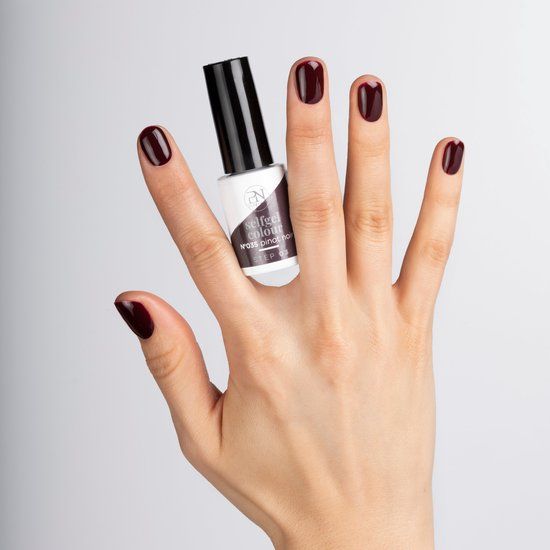 Hand mit lackierten Nägeln und Nagellackflasche. Flasche mit Aufschrift "selfgel colour". Nagellackfarbe: Dunkelrot.