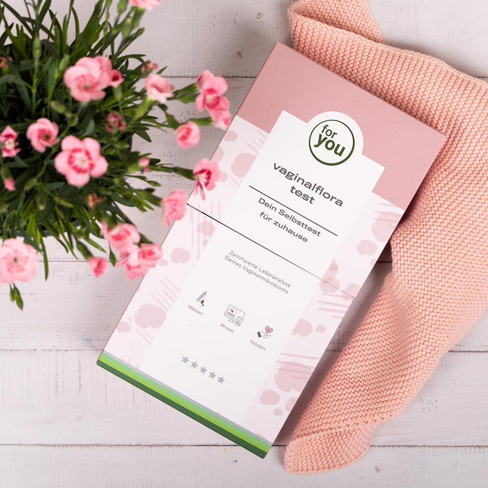 Verpackung für einen Vaginalflora Test auf einem Holztisch mit Blumen.