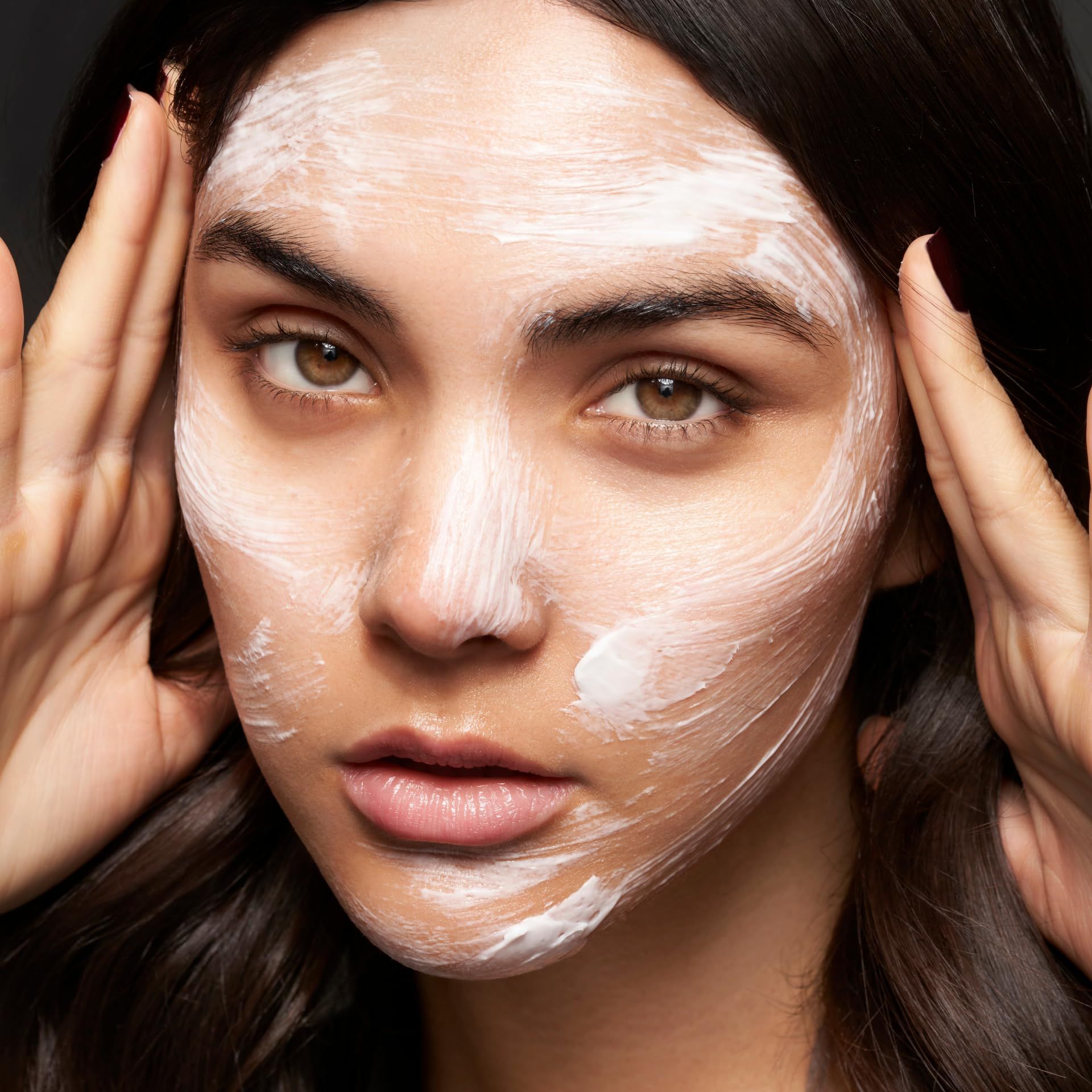 Nahaufnahme eines Gesichts mit weißer Creme. Hände berühren das Gesicht.