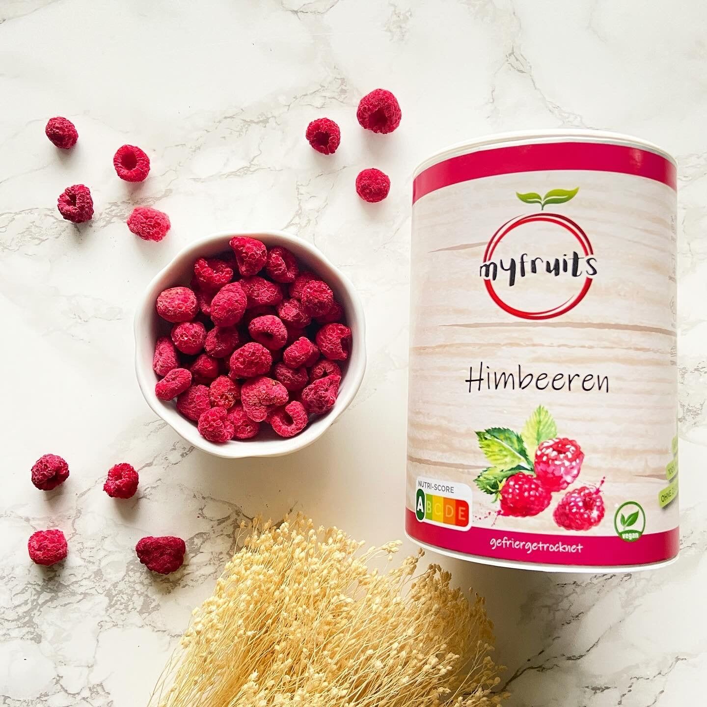 Himbeeren in Schale und verstreut. Dose mit Himbeeren-Aufdruck. Logo myfruits, Schriftzug Himbeeren. Getrocknete Beeren.