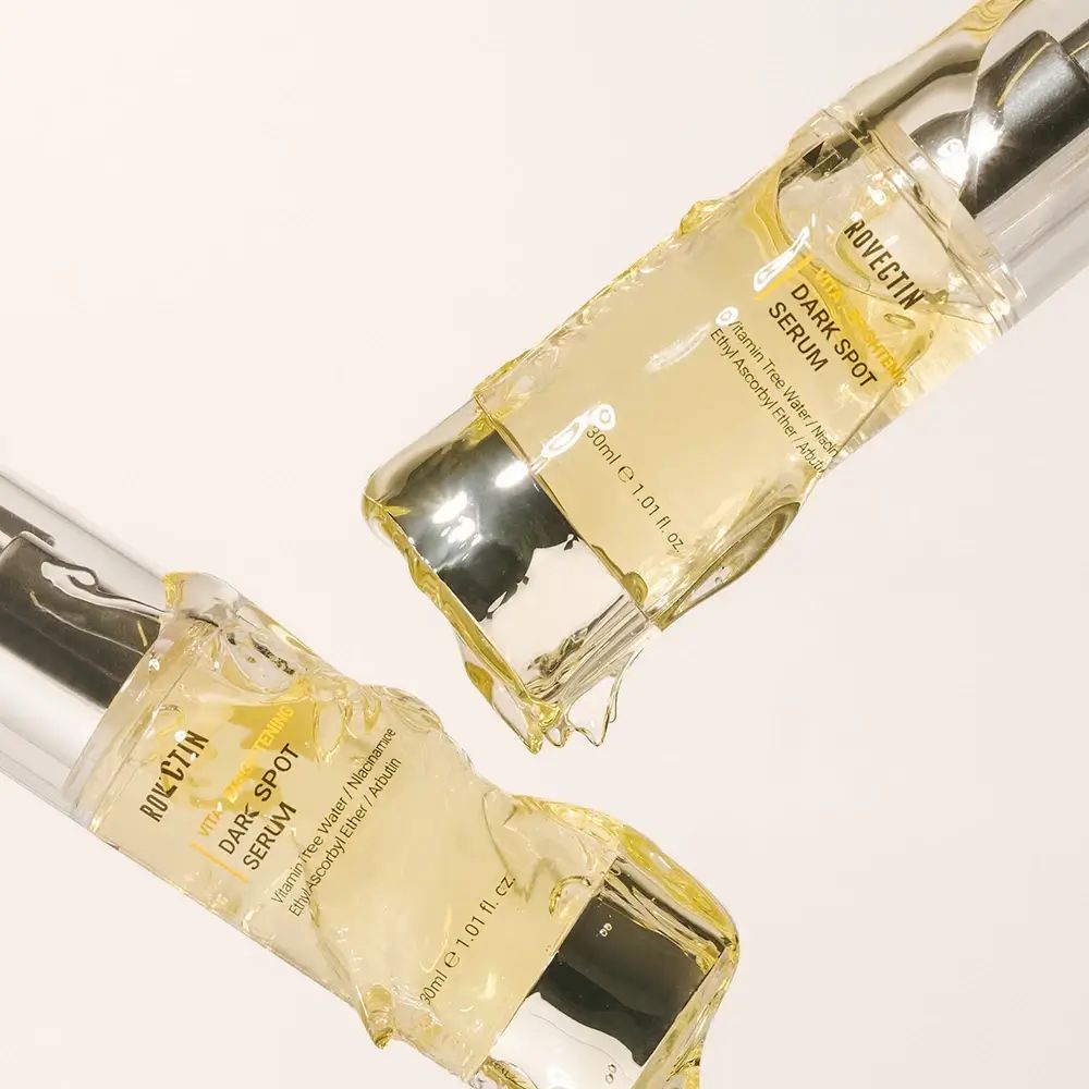 Zwei Serumflaschen mit Pumpe, teilweise mit gelber Flüssigkeit bedeckt. Aufschrift: ROVECTIN Dark Spot Serum.