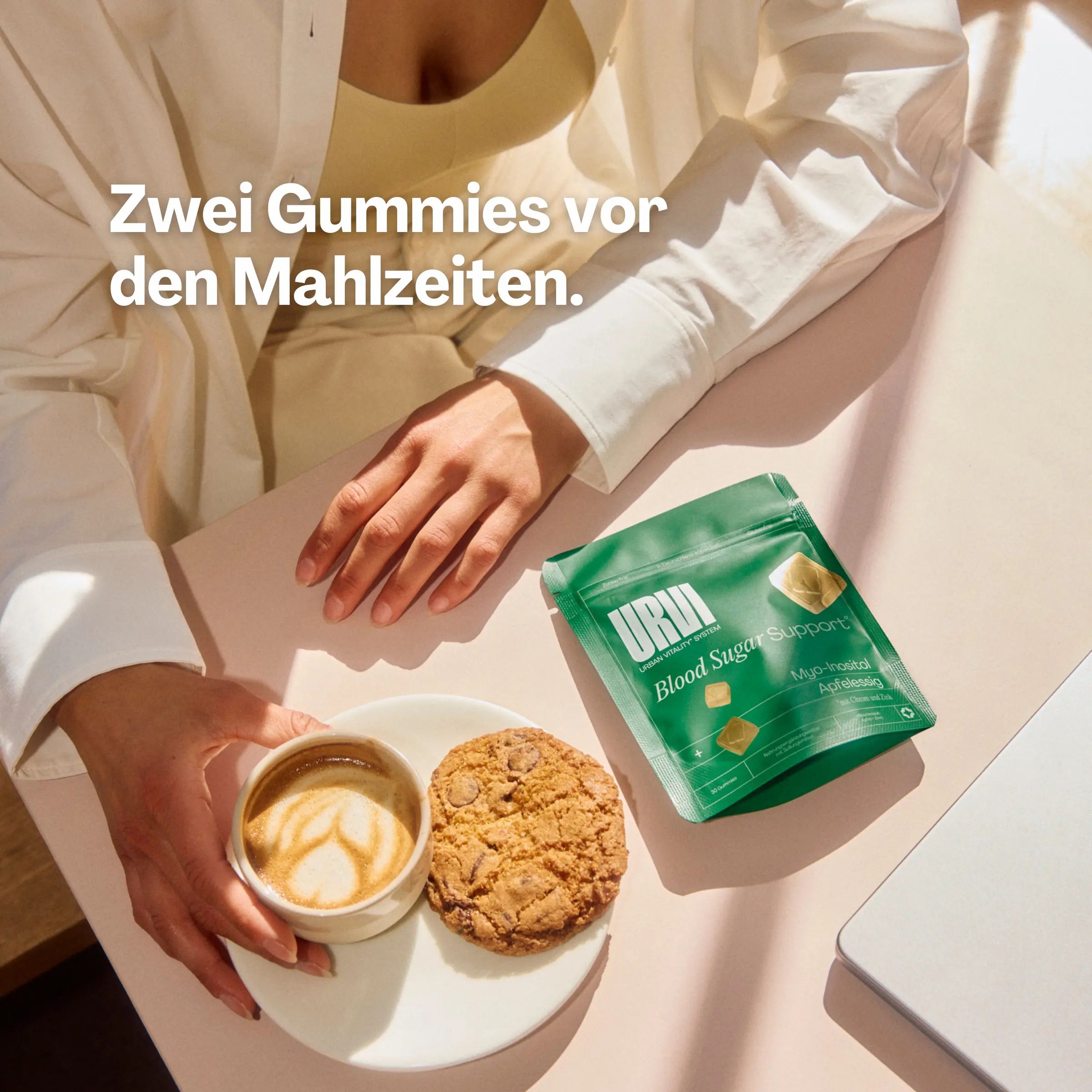 Person am Tisch mit Kaffee, Keks und einer Packung URVI Blood Sugar Support Gummies.