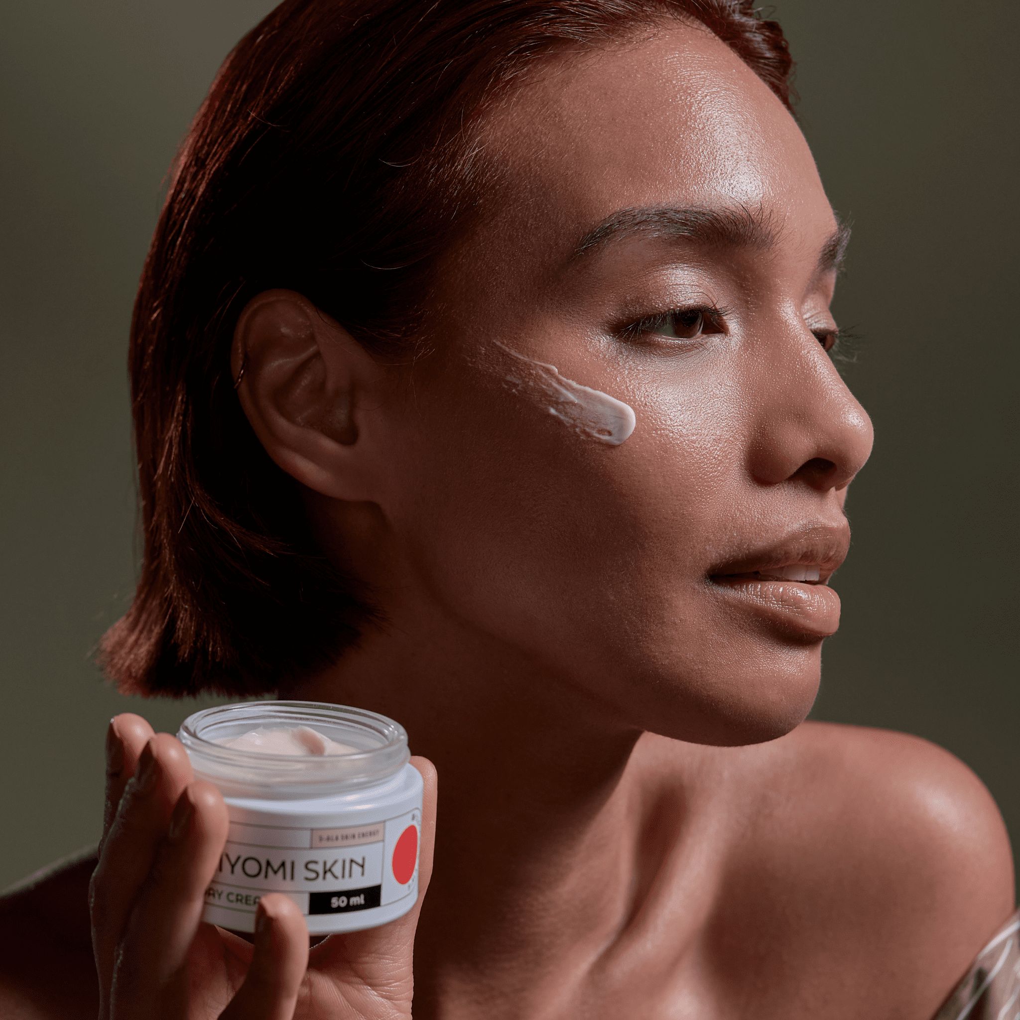 Frau mit Creme auf der Haut. Creme-Dose mit Aufschrift KIYOMI SKIN DAY CREAM. Roter Punkt. 50 ml.