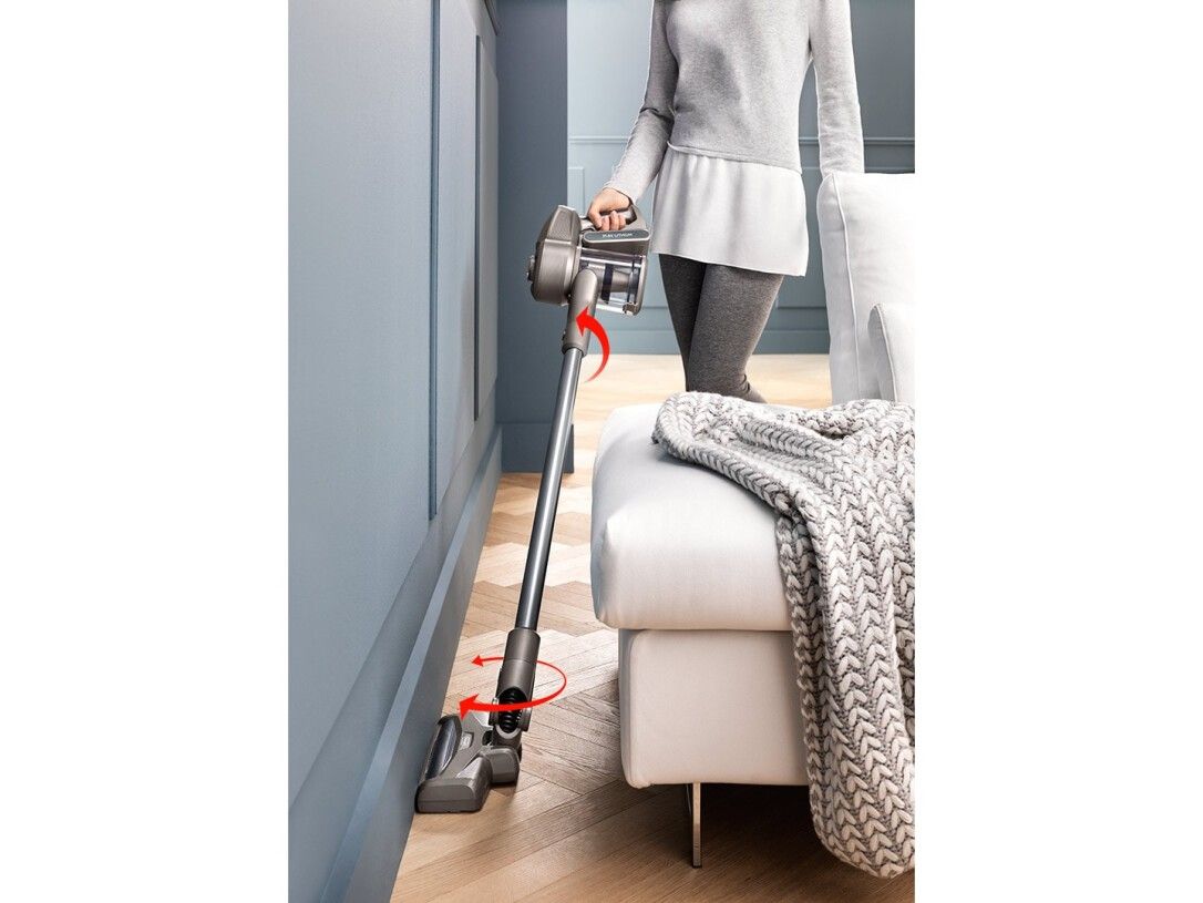 Frau benutzt einen Handstaubsauger an einer Wand. Der Staubsauger ist silberfarben.