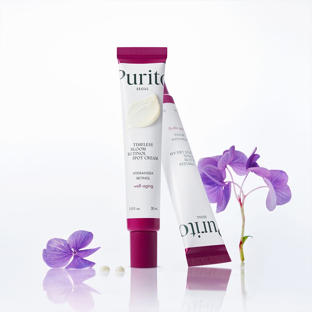 Zwei Purito Retinol Spot Cream Tuben mit Blüten.