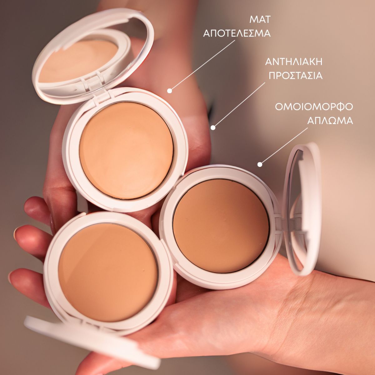 Drei geöffnete Kompaktcremes in verschiedenen Farbtönen. Aufschrift in Griechisch: MAT, ANTHLIAKI PROSTASIA, OMOIOMORFO APLOMA.