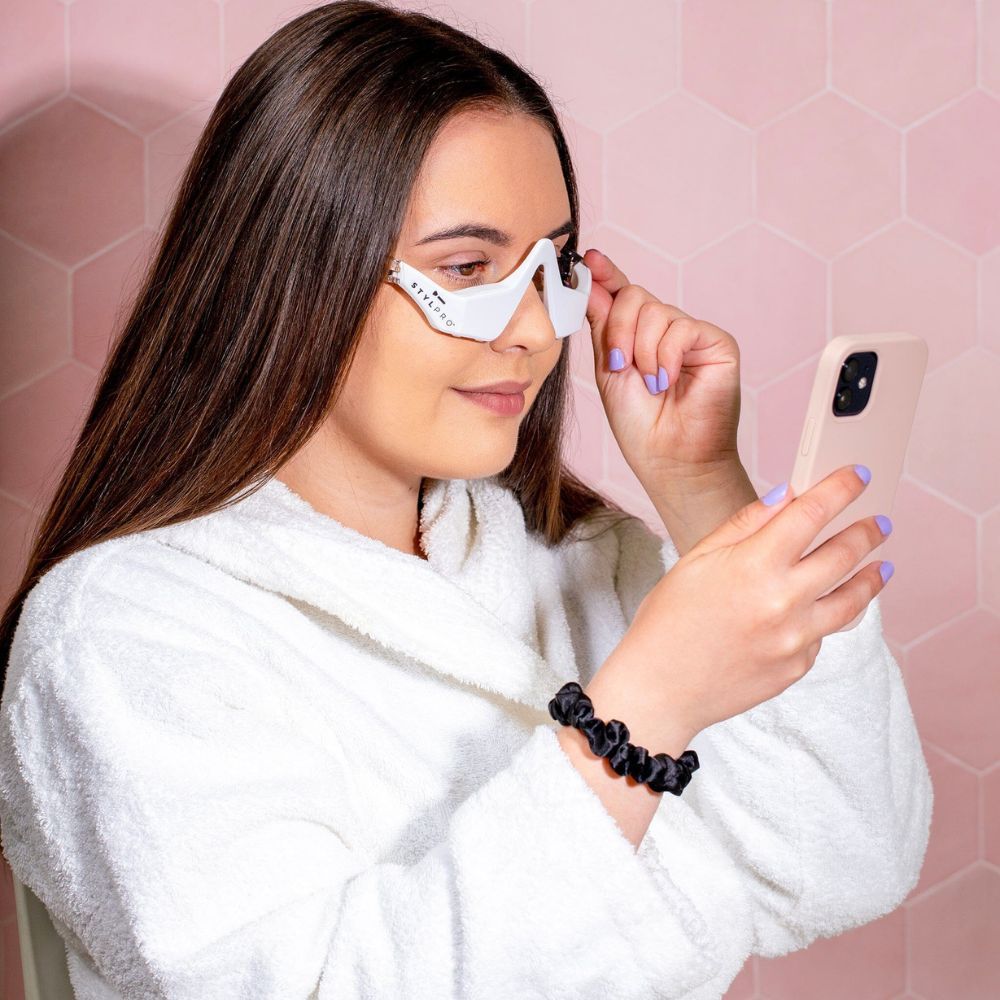 Eine Frau mit einem weißen Augenmasken-Gerät und einem Smartphone.