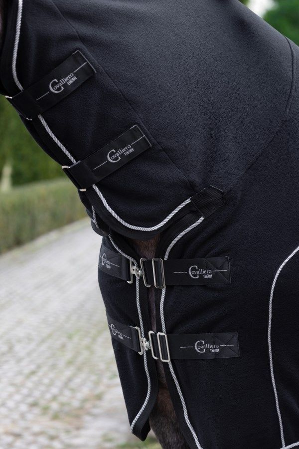Nahaufnahme der schwarzen Fleecedecke. Silberne Schnallen, weiße Paspelierung. Schwarze Etiketten mit 'Covalliero Therm'.