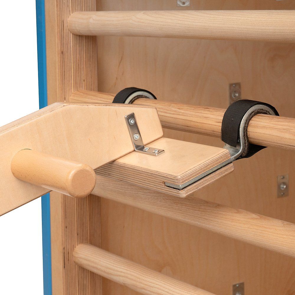 Holz-Kombigerät mit Stiften und Metallwinkel. Schwarze Gurte. Befestigt an einer Sprossenwand. Helle Holzfarbe.