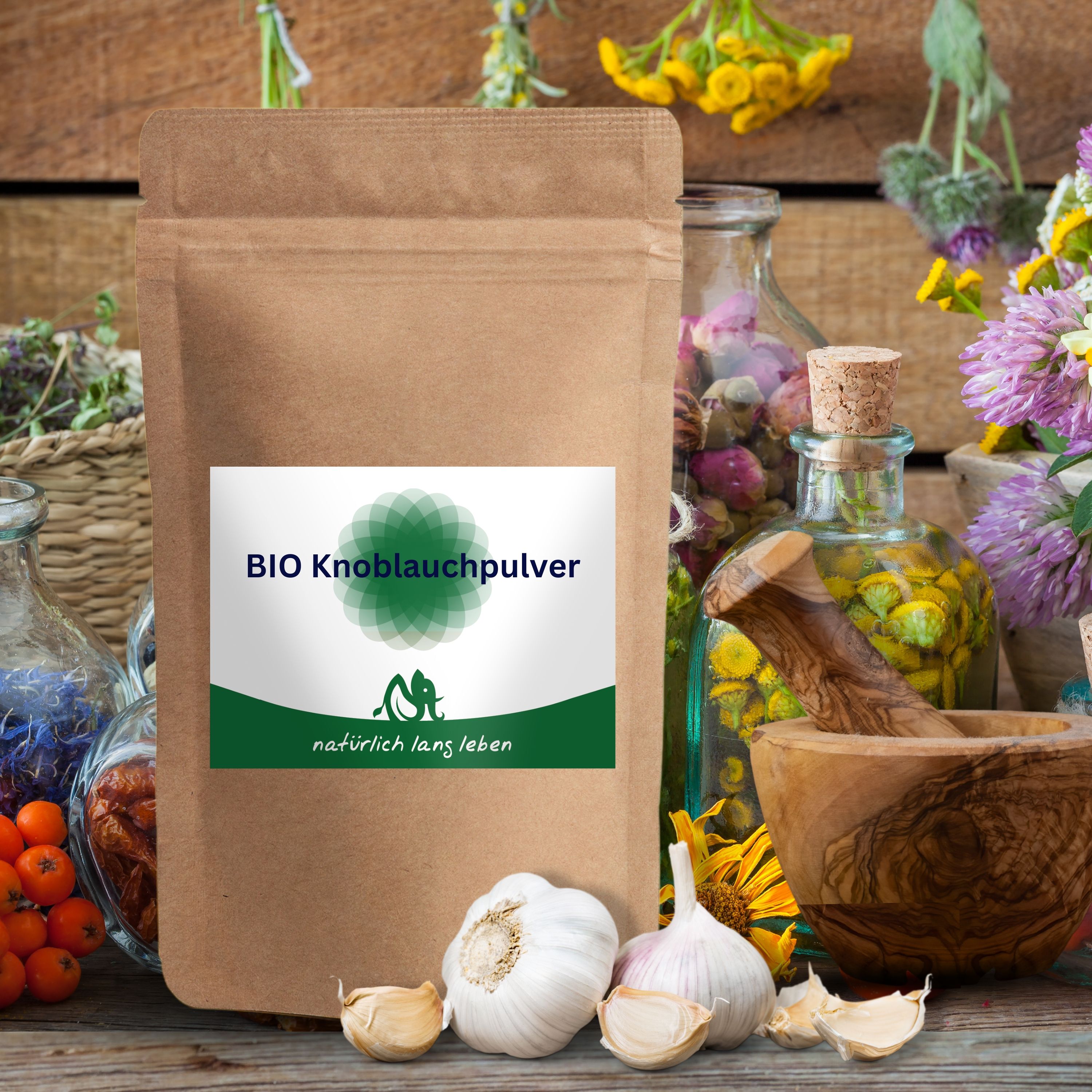 BIO Knoblauchpulver-Beutel vor Kräutern und Knoblauchzehen. Braune Papierverpackung mit grün-weißem Etikett. Aufschrift: BIO Knoblauchpulver und natürlich lang leben.