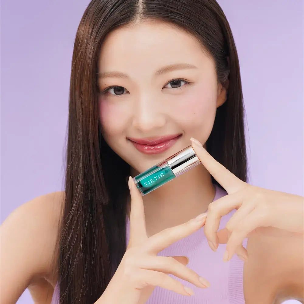 Frau hält ein Lip Oil. Das Produkt hat eine grüne Flüssigkeit und einen silbernen Deckel. Der Markenname ist sichtbar.