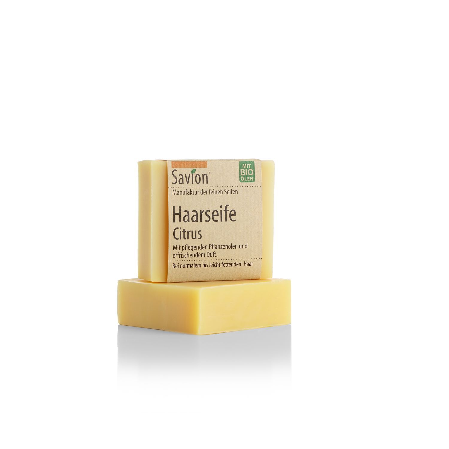 Zwei gelbliche Seifenstücke. Das vordere hat eine Papierbanderole mit Produktinformationen: Savion Haarseife Citrus, mit Bio-Ölen.