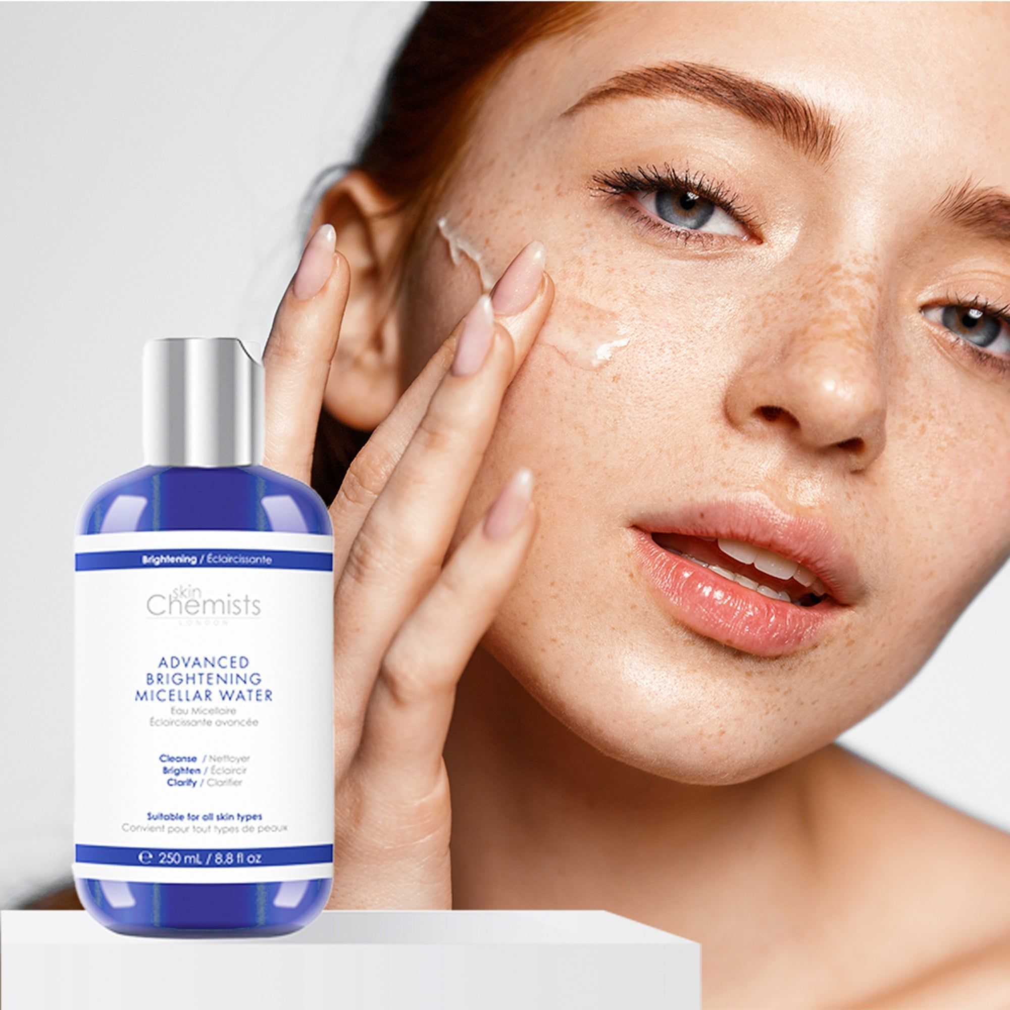 Frau trägt das Produkt auf. Blaue Flasche mit silbernem Deckel. SkinChemists Advanced Brightening Micellar Water.