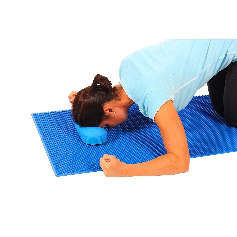 Blaue Massagematte. Frau liegt auf dem Bauch, Kopf auf blauem Kissen. Arme angewinkelt.