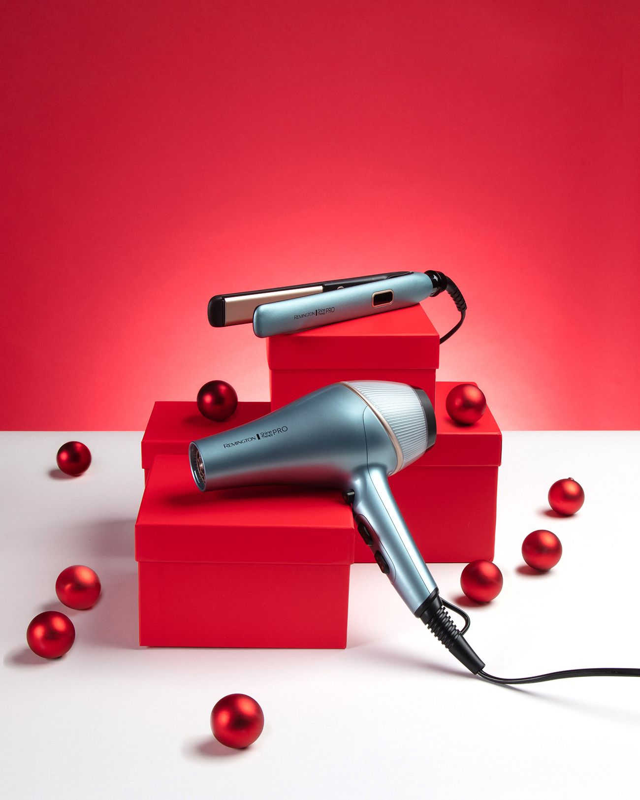 Remington Haartrockner und Glätteisen in Türkis auf roten Geschenkboxen, dekoriert mit roten Kugeln.