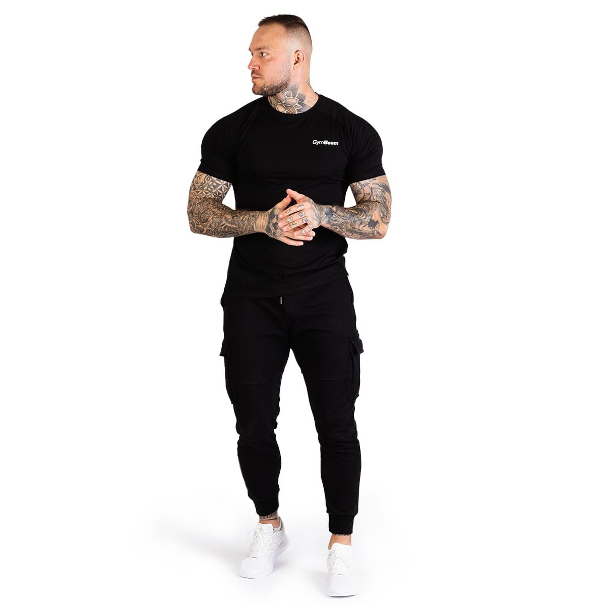 Mann in schwarzem GymBeam T-Shirt und Cargohosen, steht frontal, Hände in den Taschen.