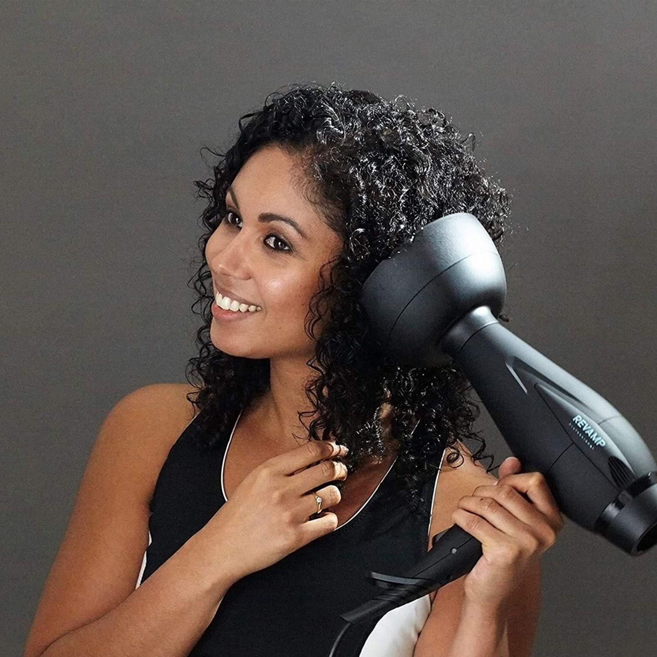 Frau mit Locken, die einen schwarzen Haartrockner benutzt. REVAMP-Logo sichtbar.